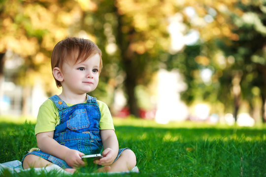 cute baby is playing with phone on the green grass