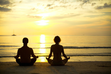 Young couple sitting on the beach in lotus position