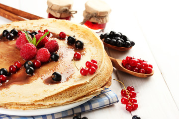 Delicious pancakes with berries and jam on plate on wooden