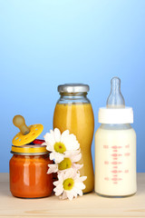 Baby food, bottle of milk, puree and juice on blue background