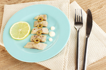 Dish of herring and lemon on plate on wooden table close-up