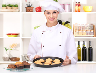 Young woman chef with cakes on dripping pan in kitchen