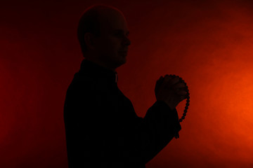 Young pastor with wooden rosary, on dark red background