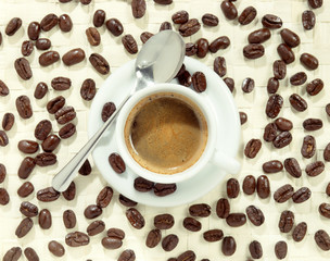 Cup of foamy coffee surrounded by coffee beans