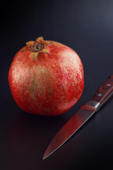 Pomegranate and knife on black background