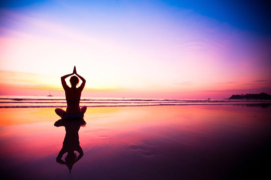 Silhouette of a woman meditating on the beach at sunset