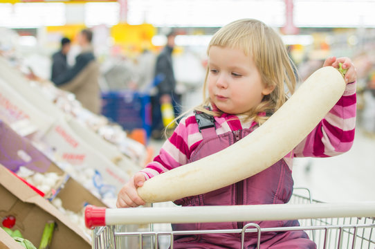 Adorable girl with daikon radishe in shopping cart in supermarke
