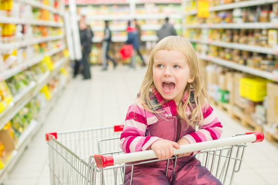 Adorable girl screaming in shopping cart in supermarket