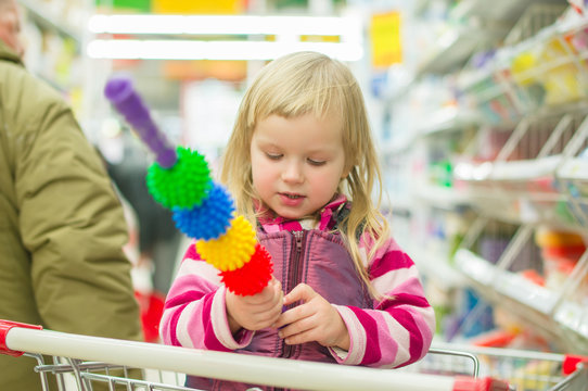 Adorable girl with massage tool in shopping cart in supermarket