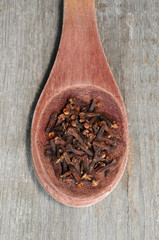 Cloves in wooden spoon on rustic wooden background