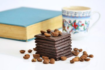 Chocolate with coffee beans and unfocused cup of coffee and book