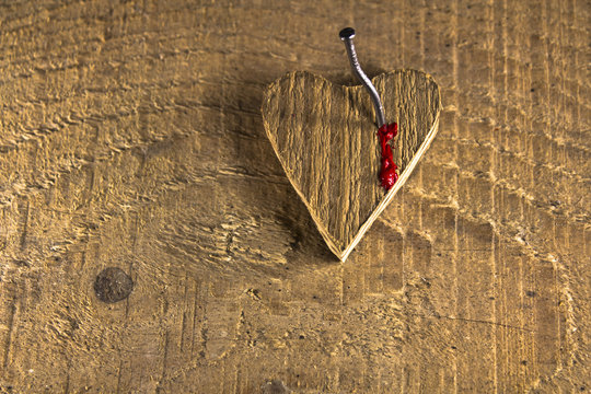 Heart nailed on wooden background and bleednig