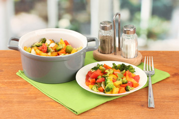 Vegetable stew in gray pot on wooden table on bright background