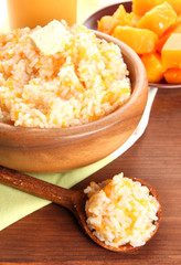 Taste rice porridge with pumpkin in bowl on wooden background.