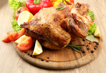 Whole roasted chicken with vegetables on plate, on wooden table