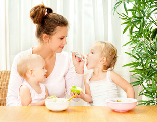 young mother feeding her two daughters from a spoon