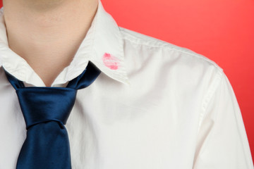 Lipstick kiss on shirt collar of man, on red background