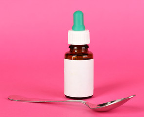 Medical drops and spoon for them on pink background