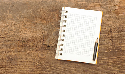 A white notebook with pencil on a wooden desk