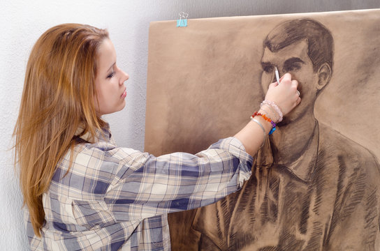 Young female artist drawing man portrait in her art studio