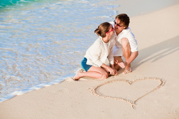 Fototapeta premium portrait of young happy couple drawing a heart on the sand