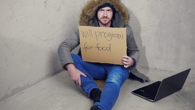 homeless man sitting on the floor with a sign
