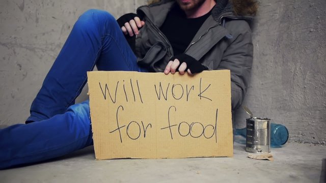 homeless sitting on the floor with a cardboard and a tin