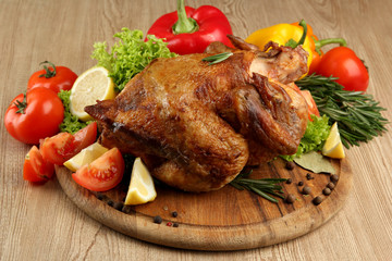 Whole roasted chicken with vegetables on plate, on wooden table