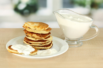 Sweet pancakes on plate with sour cream on table in kitchen