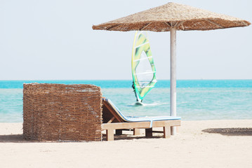 beach chair with straw sunshade at the sea and windsurfer