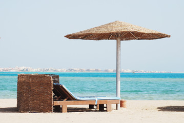 empty beach chair with straw sunshade at the sea