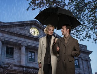 Elegant couple with umbrella against building facade