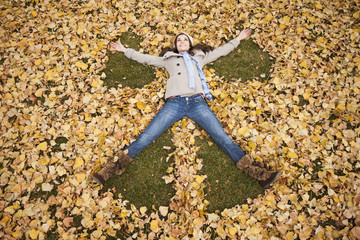 Caucasian woman making angel in autumn leaves