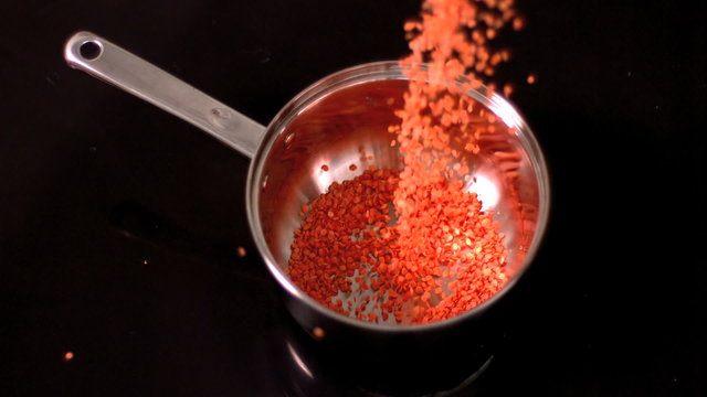 Red lentils falling into pot on black background