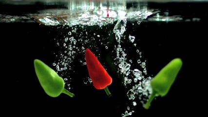 Chili peppers falling in water in slow motion - Powered by Adobe