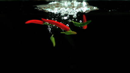 Red and green chili peppers falling into water in slow motion - Powered by Adobe