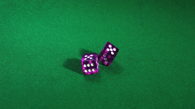 Purple dice rolling on green table in slow motion