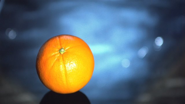 Orange falling into blue water and floating in slow motion