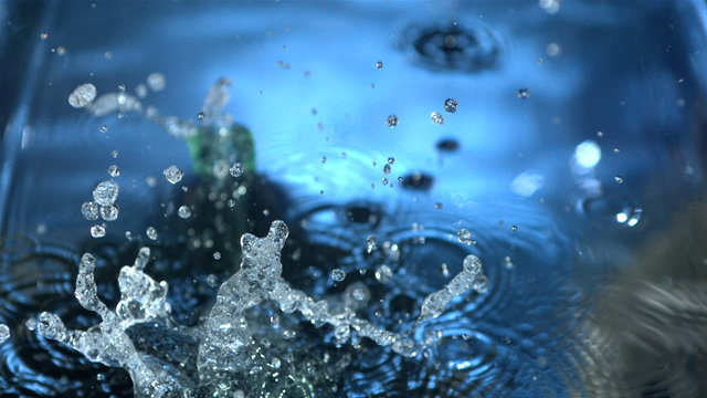 Glass bottle falling into blue water in slow motion
