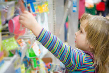 Adorable girl select toys on shelves in supermarket