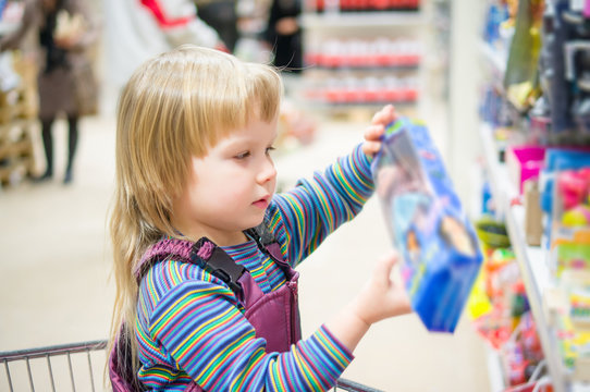 Adorable girl select toys on shelves in supermarket