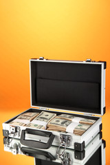 Suitcase with 100 dollar bills on orange background