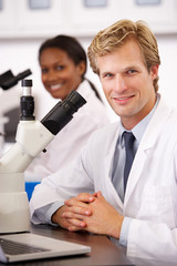 Male And Female Scientists Using Microscopes In Laboratory