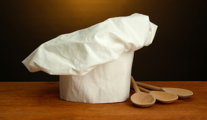 Chef's hat with spoons on table on brown background