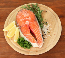 Fresh salmon steak on cutting board, on wooden background
