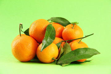 Ripe sweet tangerines with leaves, on green background