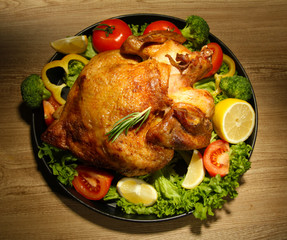 Whole roasted chicken with vegetables on plate, on wooden table