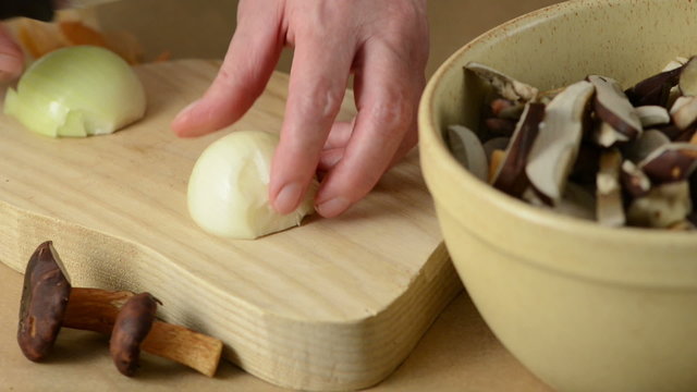 Slicing onion on a board aside cup of Bay Bolete mushrooms