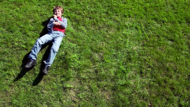 Little boy lay on grass plot and then rolls away