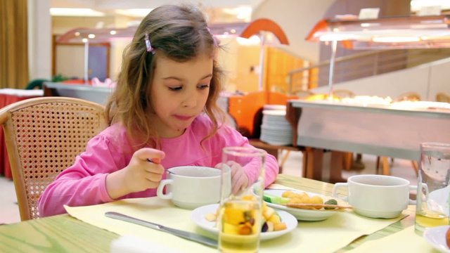 Little girl sits at table and eats breakfast in cafe
